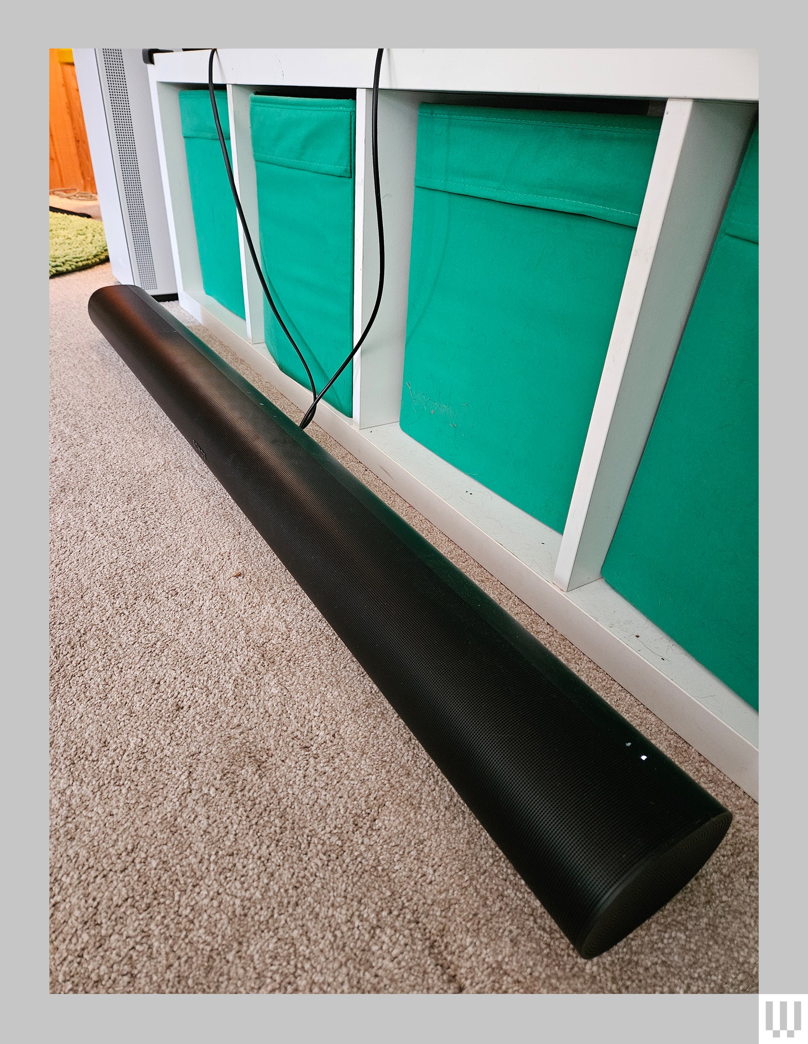 Black long tube shaped speaker on carpeted floor next to a credenza