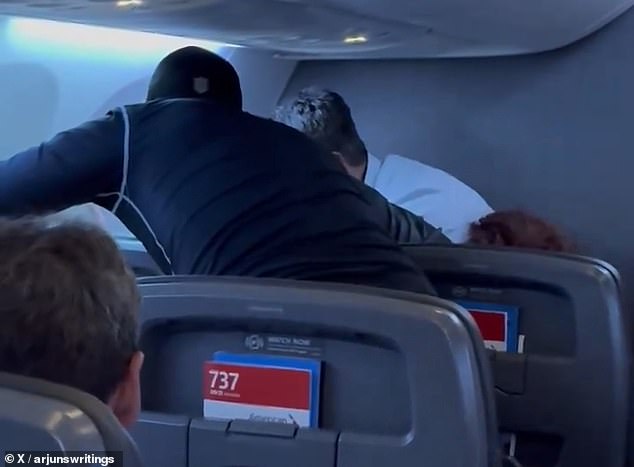 Video shared online shows several men leaning over a man sitting in the front row of the flight from Miami, Florida to Charlotte, North Carolina, on Wednesday, October 2.