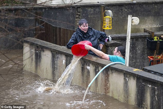 People pour water from their front garden in Pontypridd, Wales, as officials declare a serious incident due to river flooding.