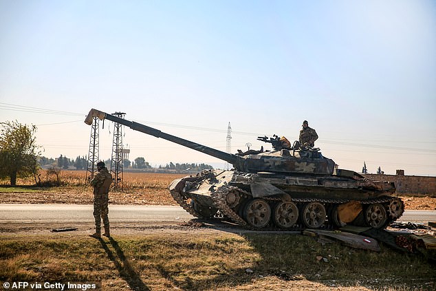 An anti-government fighter stands near a Syrian regime tank that was abandoned along a road in the eastern part of Aleppo province on December 1, 2024. Syrian rebels took over Aleppo and expelled government forces