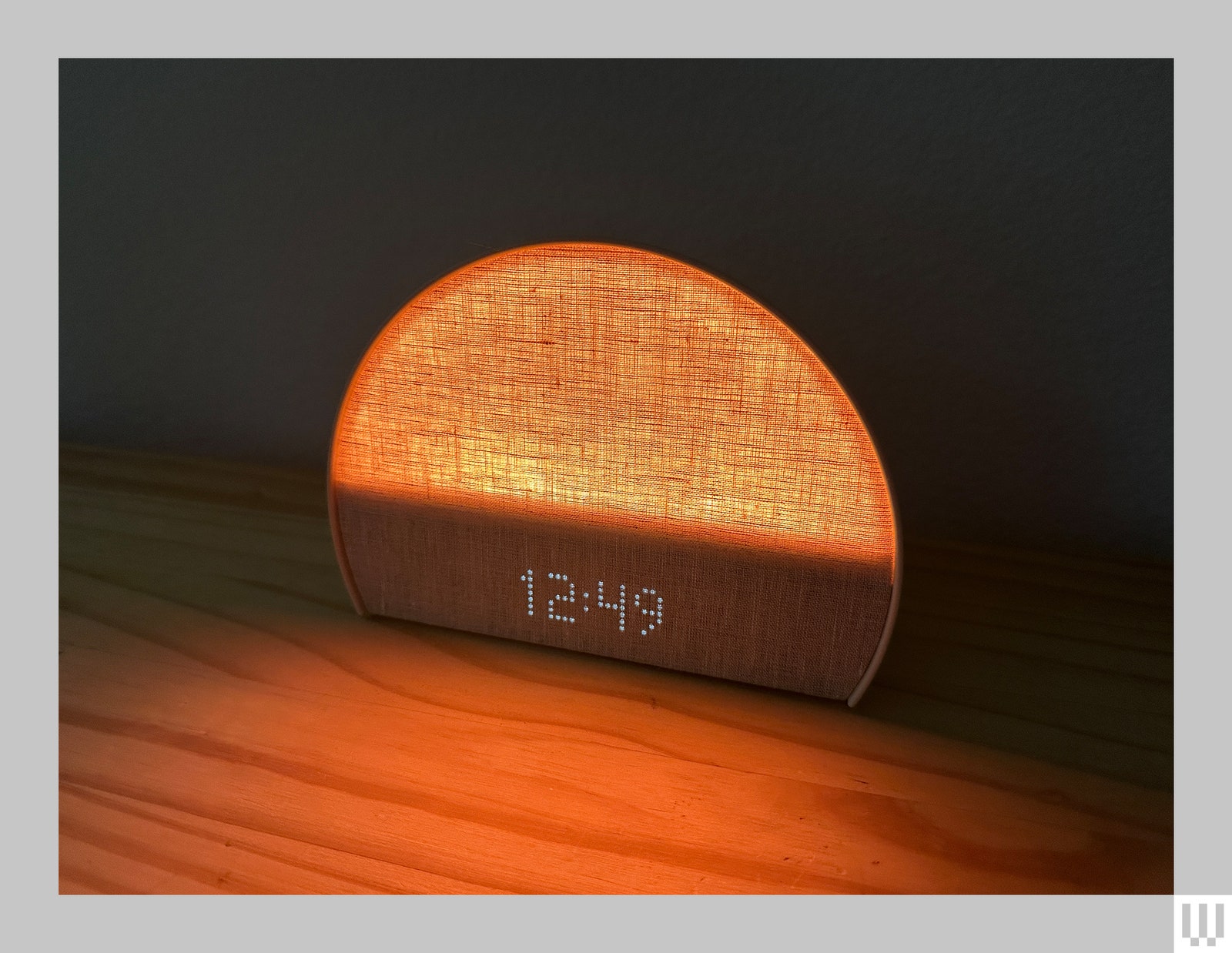 Semicircle shaped alarm clock with fabric cover on top and digital numbers below.