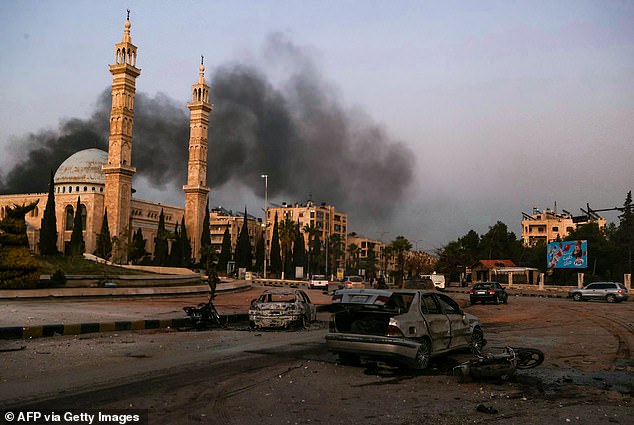 Smoke rises in the distance as damaged cars are seen at the site of Syrian regime airstrikes on anti-regime fighters in Aleppo, northern Syria, on November 30, 2024.