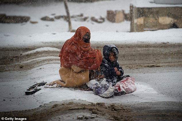 An Afghan woman begs for money from passing cars in the snow, with a child curled up next to her, on the road from Kabul south towards Pul-e Alam, Afghanistan, on January 17, 2022.