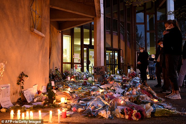 People stand in front of flowers and candles next to a sign that says 