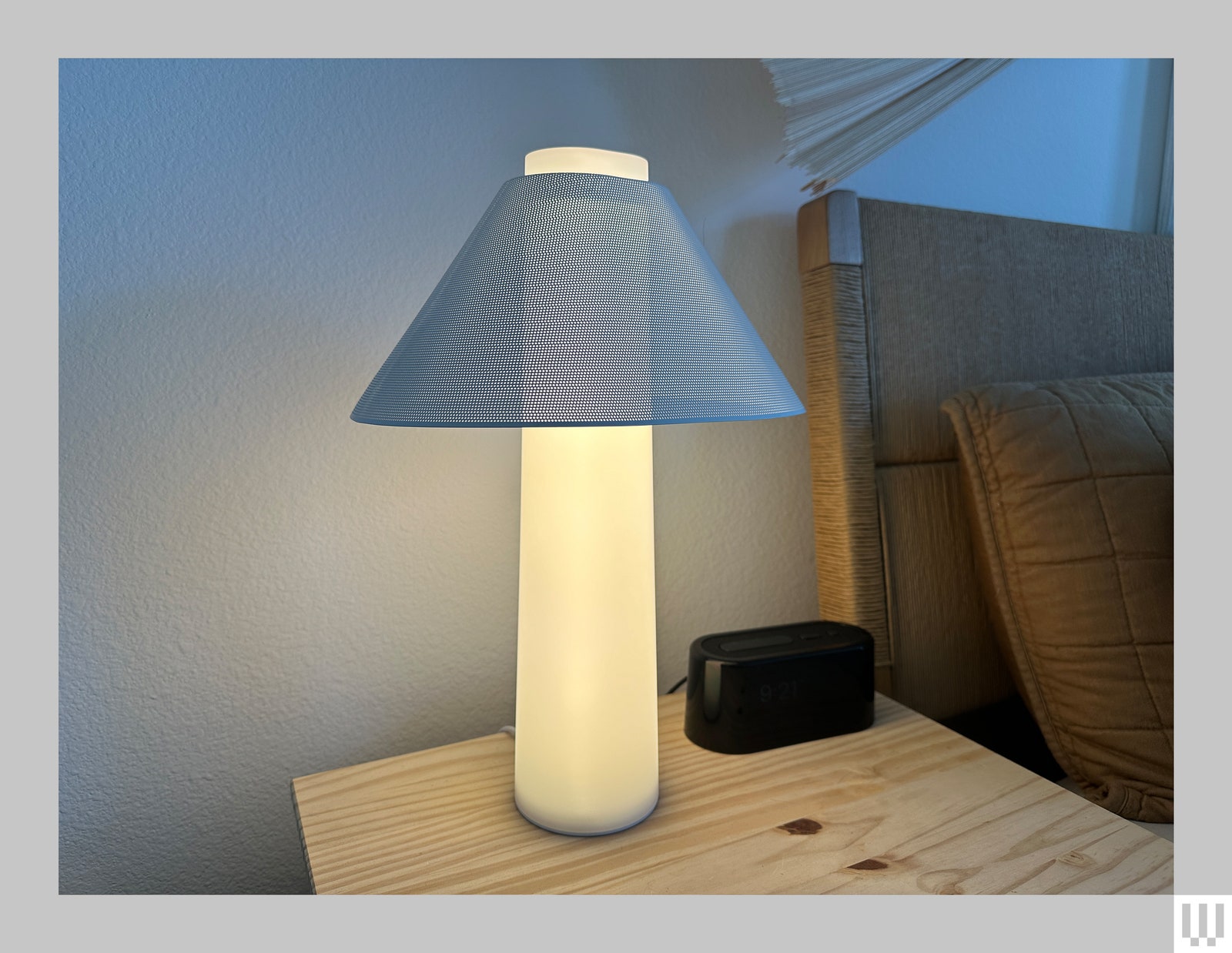 Loftie Lamp a bright cylindrical lamp with a blue mesh shade placed on a wooden bedside table