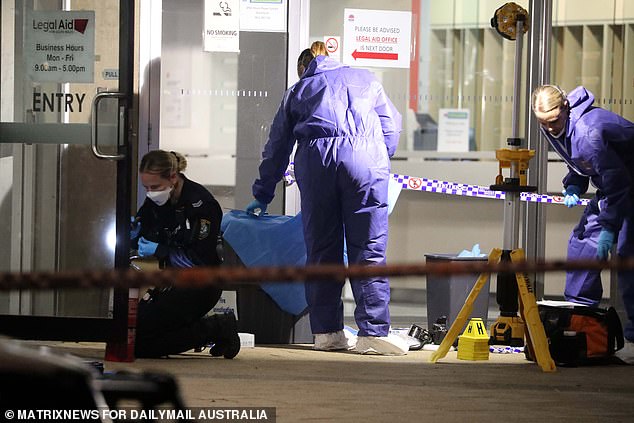 Pictured: A forensic officer photographs and packages evidence outside the Legal Aid building on Thursday evening.