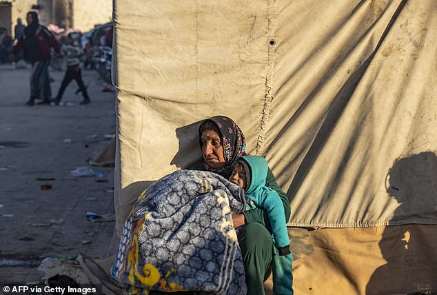 A Syrian Kurdish woman, fleeing northern Aleppo, waits on a street with a child upon arrival in Tabqa, on the western outskirts of Raqa, on December 4, 2024.