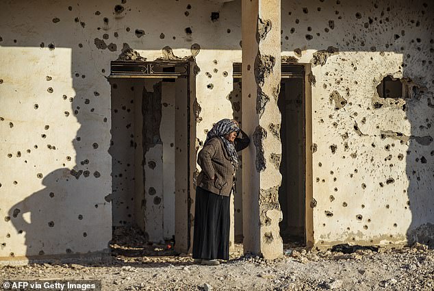 A Syrian Kurdish woman, fleeing northern Aleppo, leans against a bullet-riddled wall as she arrives in Tabqa, on the western outskirts of Raqa, on December 4, 2024.