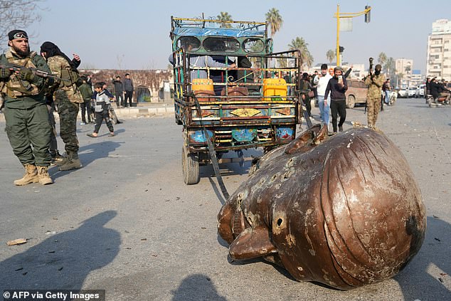 A truck drags the head of another toppled statue of the late Syrian President Hafez al-Assad through the streets of the city of Hama on December 6.