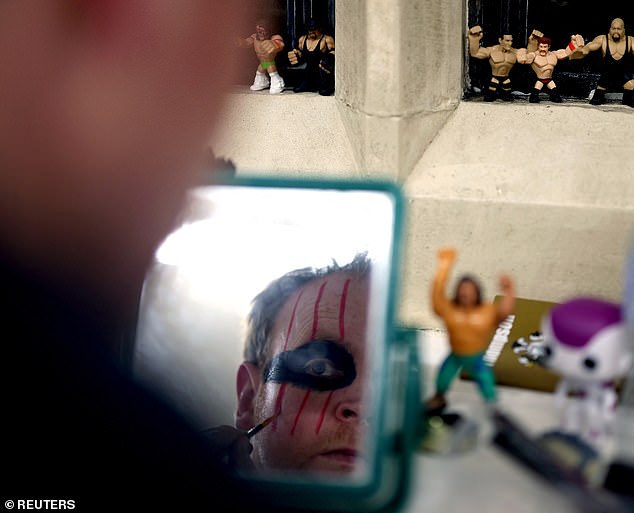 A male wrestler prepares with colorful face paint in a backstage dressing room.