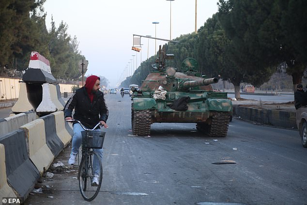 A man sits on a bicycle next to a tank in Homs, Syria, on December 8.