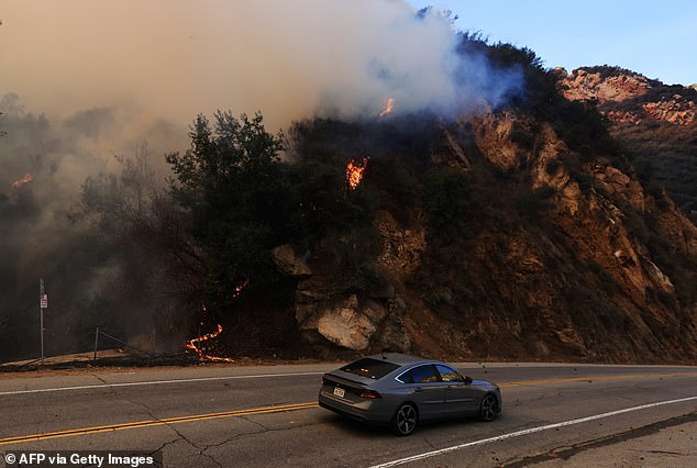 A motorist passes as a mountainside burns as the Franklin Fire grows in Malibu, which after more than half a day is still not in the slightest under control