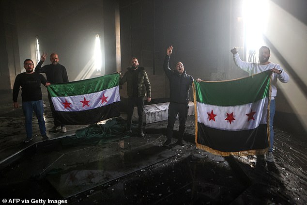 Rebel fighters hold the Syrian flag at the burned grave of late Syrian President Hafez al-Assad.