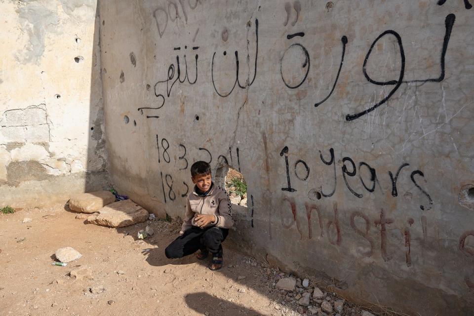 A boy sits next to the wall where Muawiyah graffiti first angered authorities in 2011 (Bel Trew/The Independent)