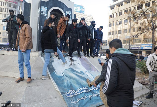 People kick down a sign depicting Syrian President al-Assad after the Syrian army command notified officers that his 24-year authoritarian rule had ended.