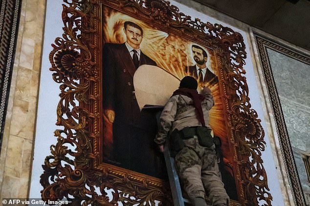 An anti-regime fighter tears down a banner depicting Syrian President Bashar al-Assad (L) and his brother Maher at the airport in the northern Syrian city of Aleppo on December 2, 2024.