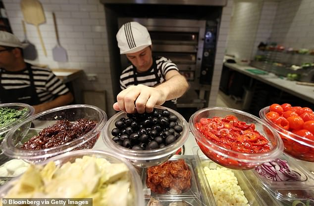 Pictured: Pizza ingredients are placed in glass bowls as an employee garnishes pizzas in the kitchen of a PizzaExpress restaurant in London.