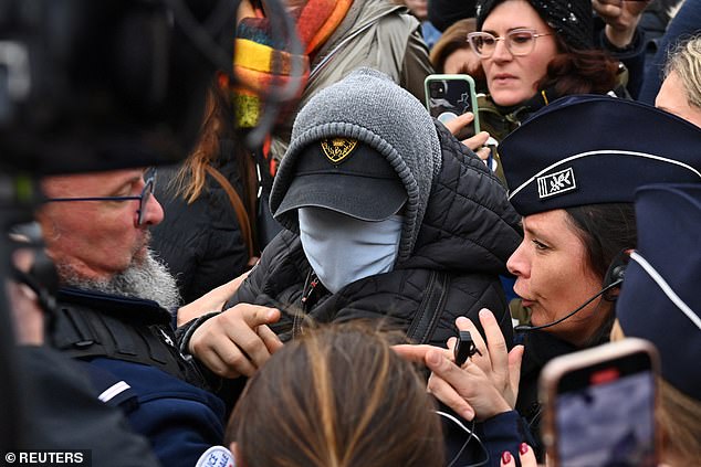 A man hiding his face is surrounded by French police, journalists and protesters as he leaves after the verdict in the Dominique Pelicot trial.