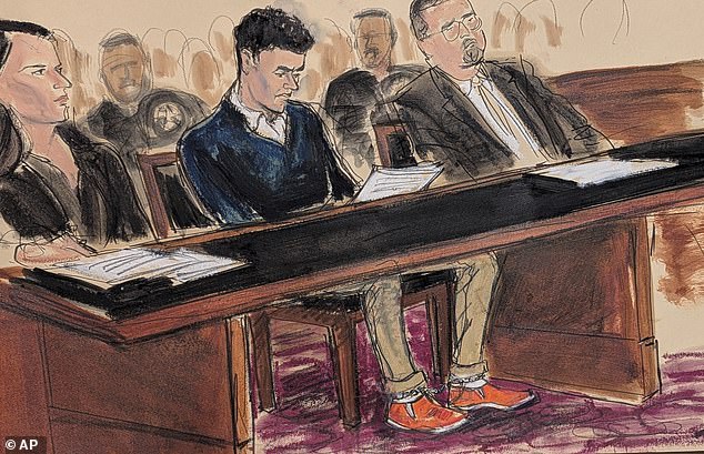 Mangione, center, sits in court reading the federal complaint while wearing orange slip-on shoes and his ankles shackled in Manhattan federal court