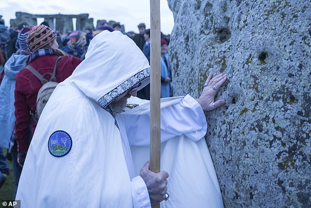 A man places his hands on one of the stones during the winter solstice celebrations at Stonehenge today.