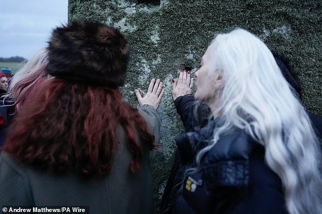 People touch one of the stones as they take part in winter solstice celebrations during sunrise at the Stonehenge prehistoric monument.