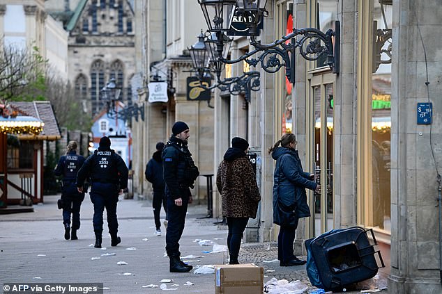 Overturned wheelie bins and debris are seen as police officers walk through a closed Christmas market where a car crashed into a crowd, injuring more than 60 people the night before.