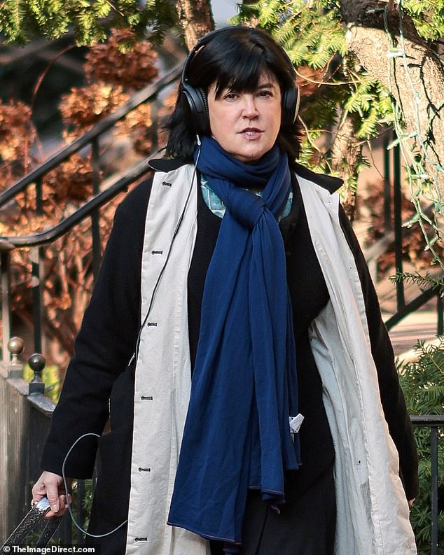 She was wearing a long black winter coat with beige lining over a black dress with a dark blue scarf tied in front.