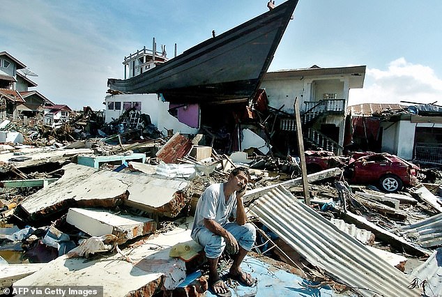 A man sits in front of a boat dragged onto the roof of a building on December 26, 2004.