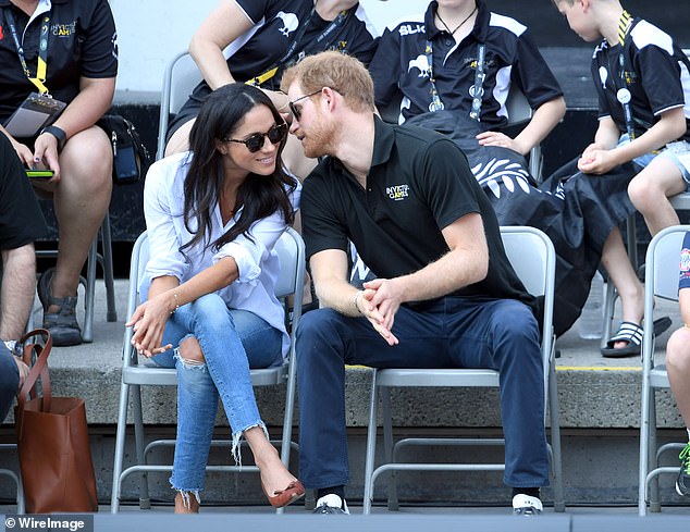 The Prince whispering to Meghan, who is wearing a Misha Nonoo's Husband t-shirt