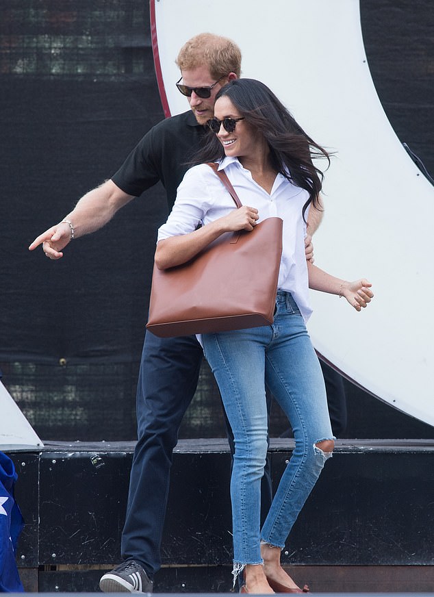 Harry guiding Meghan during their first official appearance together; she is wearing ripped jeans and sunglasses.