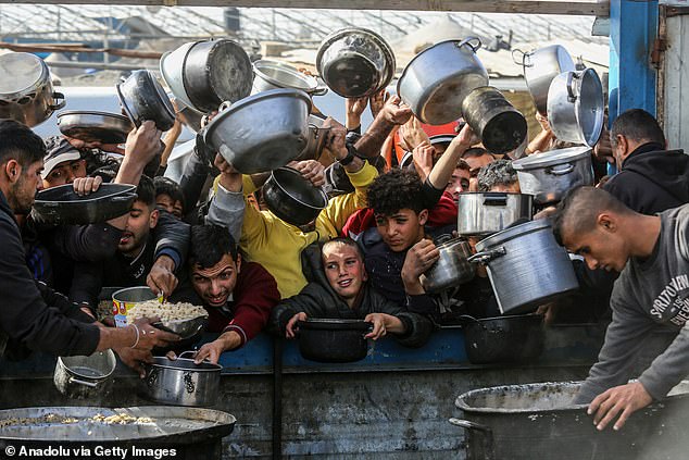 Palestinians line up with empty pots to receive meals distributed by charity organizations as people struggle with hunger due to the embargo imposed by Israeli forces on December 26, 2024 in Khan Yunis, Gaza