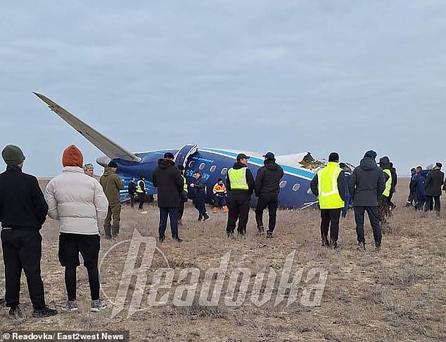 People are seen standing near the back of the crashed passenger plane.