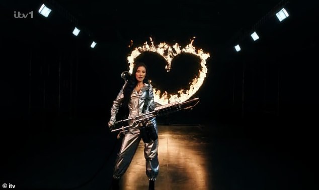 During the new teaser video, the TV host appeared in a silver hooded jumpsuit and silver mask, wielding a flamethrower and lighting up a heart-shaped ring.