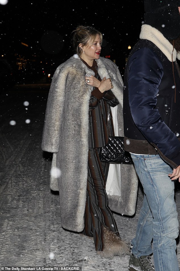 She modeled a stylish fur coat atop a brown and gray striped jacket and matching pants as she walked through the drifting snow.