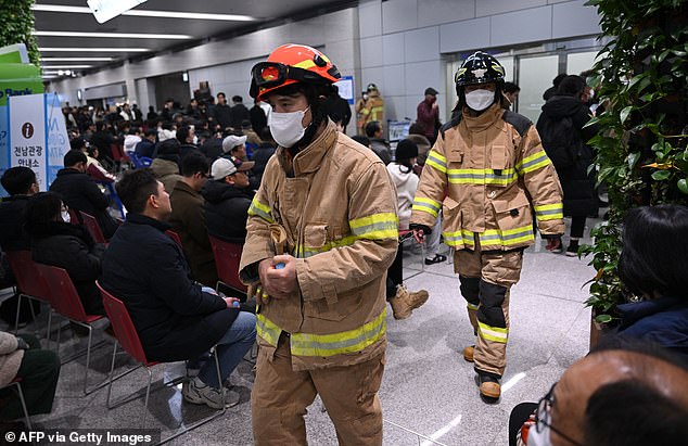 Firefighters walk past people and families of passengers of the crashed Jeju Air Boeing 737-800 series plane at Muan International Airport in South Jeolla province.