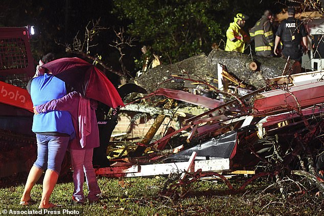 Bystanders embrace as first responders try to free a victim after a tree fell on a home in Natchez, Miss., Saturday, Dec. 28, 2024