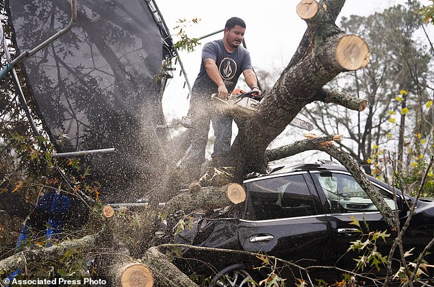 Saul Rodriguez uses a chainsaw to remove debris on top of a car from a woman's home after strong thunderstorms moved through the Greater Houston area, Saturday, Dec. 28, 2024, in Porter Heights