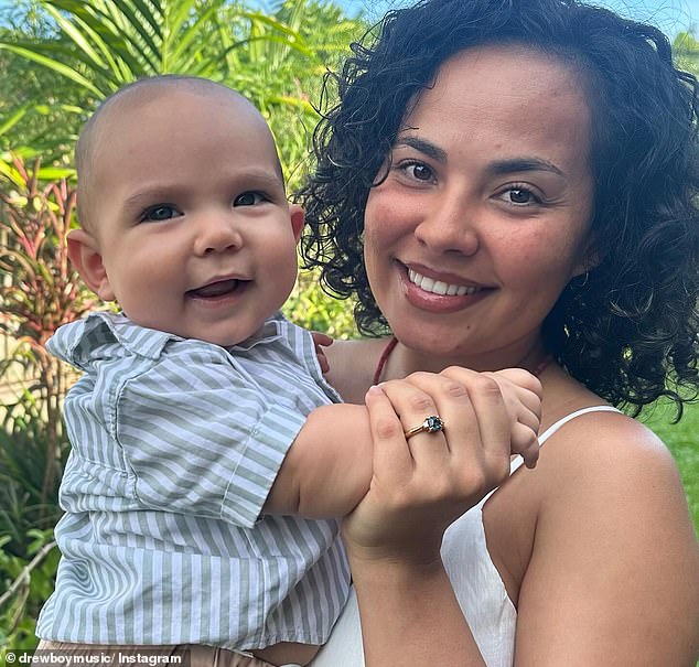 She beamed in another photo showing off her statement engagement ring, while cuddling baby Rex, whom the couple welcomed into the world in July.