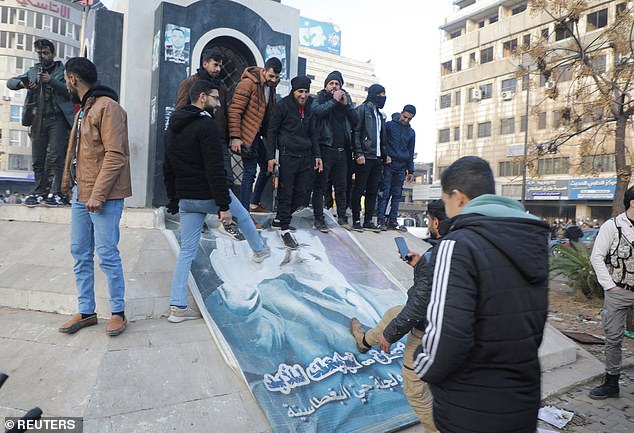 People kick down a sign depicting Syrian President Bashar al Assad after the Syrian army command notified officers that al-Assad's 24-year rule had ended.