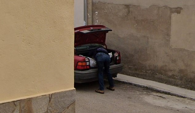 The photo shows a man carrying what appears to be a body bag into the trunk of a red car.