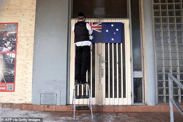 A man is seen hanging the Australian flag outside the damaged synagogue.