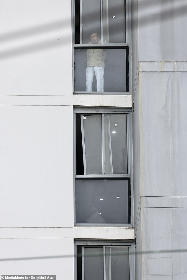 A resident is seen looking out the window of his unit as police continue their investigations.