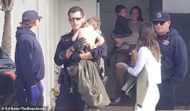 Footage of the busy scene captured by an onlooker shows Officer Warner standing outside the home on Sunset Cliffs Boulevard holding the shirtless child to his chest as his gloved hands stroke and rub the child's back