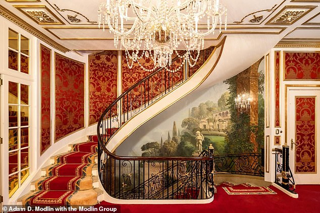 The luxurious home features a spiral staircase covered in thick deep red carpet, a formal living room with a large Italian crystal chandelier, surrounded by custom gold paneling, and ceiling heights of over 10.5 feet.