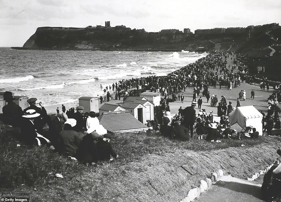 Tourists are photographed in Scarborough's North Bay in 1913. The ruins of Scarborough Castle, a medieval fortress, are seen on the hill in the back of the shot. The Scarborough Civic Society notes that the ruins 