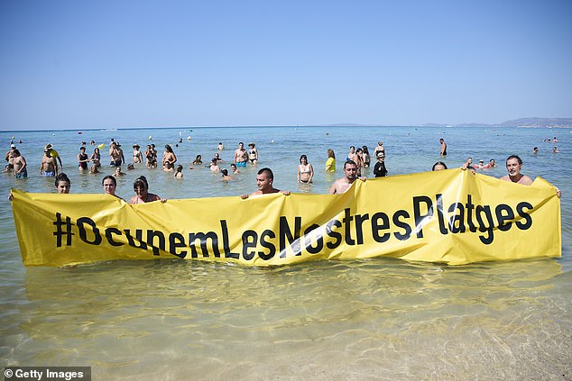 Members of the Mallorca Platja Tour association demonstrate against tourist saturation with a banner that says 'Let's occupy our beaches!' on the beach of Palma de Mallorca on August 11, 2024 in Mallorca, Spain