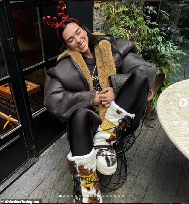 Dua Lipa showed off her holiday spirit on Christmas Eve by pairing cowhide Moon Boots with high-shine black leggings and a brown shearling coat, adding a fun touch with red reindeer ears.