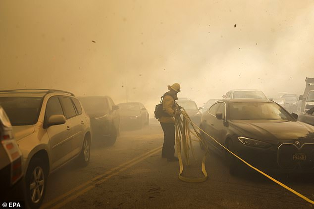 A Los Angeles firefighter drags a hose past cars trying to evacuate a neighborhood threatened by the Palisades wildfire