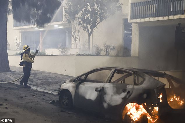 A Los Angeles County firefighter battles the Palisades wildfire as a car burns