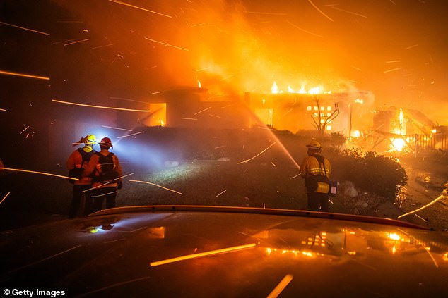 Firefighters battle flames from the Palisades Fire that set a house on fire during a powerful storm on January 8